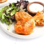 air fryer buffalo drumsticks on a white plate with salad.