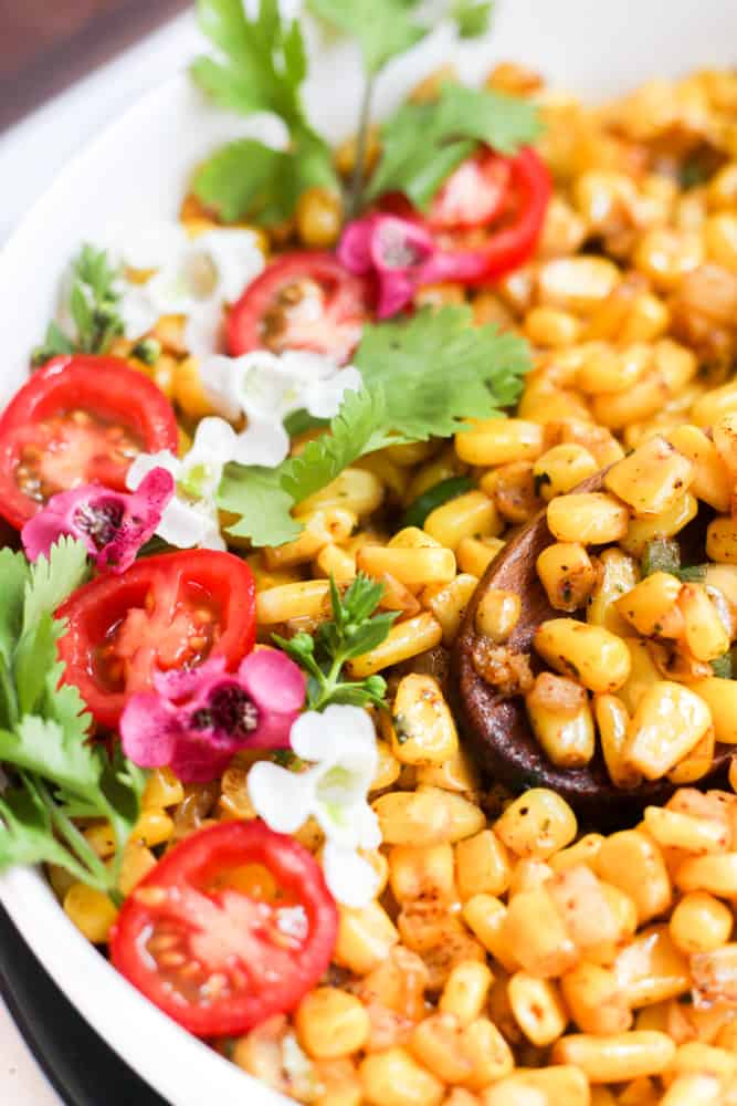 frozen corn cooked in the air fryer with tomatoes, herbs, and flowers.