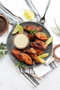 air fryer jerk chicken wings on a black plate with lime wedges.