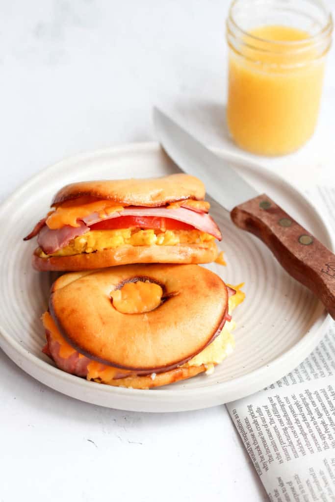 gluten free breakfast sandwich bagel on white plate with knife.