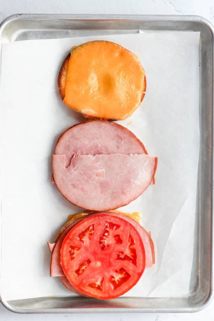 gluten free bagels topped with cheese, ham, and tomato.