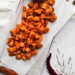 air fryer sweet potato cubes on parchment paper with bowl of salt and flowers.