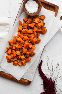 air fryer sweet potato cubes on parchment paper with bowl of salt and flowers.
