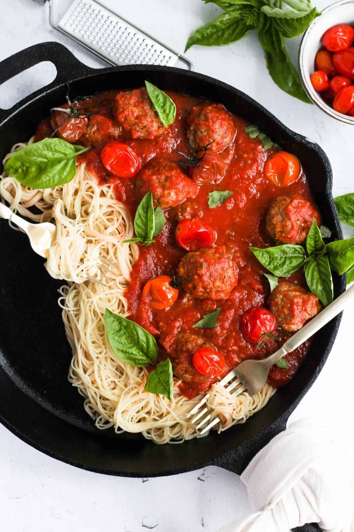 meatballs without eggs in cast iron pan with pasta, sauce, and basil.