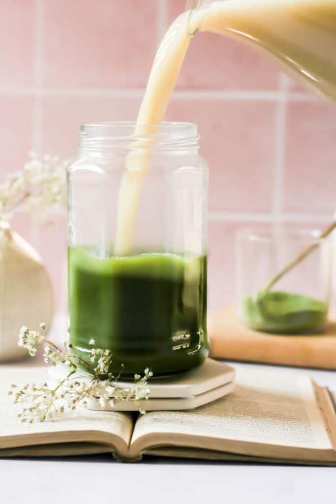 oat milk pouring into glass jar of matcha water.