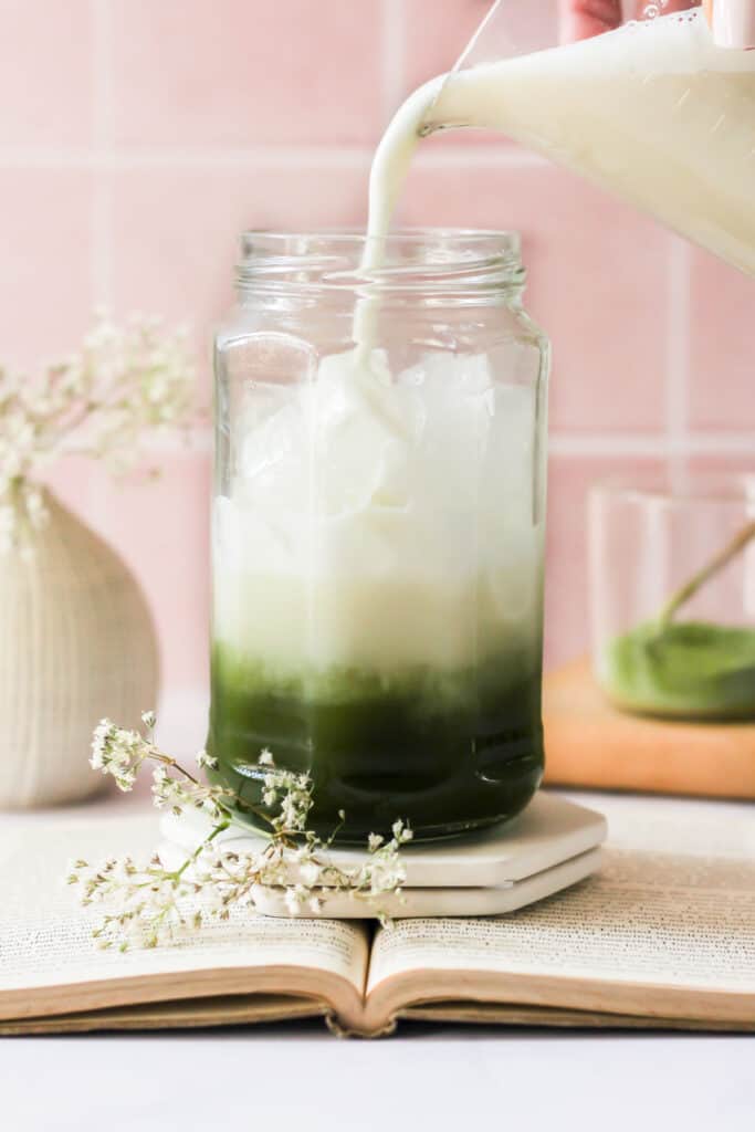 oat milk pouring into an iced matcha latte.