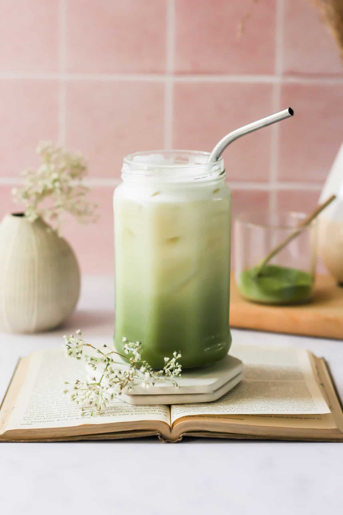 oat milk matcha latte in glass jar on a book with a silver straw.
