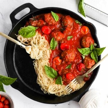 meatballs without eggs in cast iron pan with pasta, sauce, and basil.