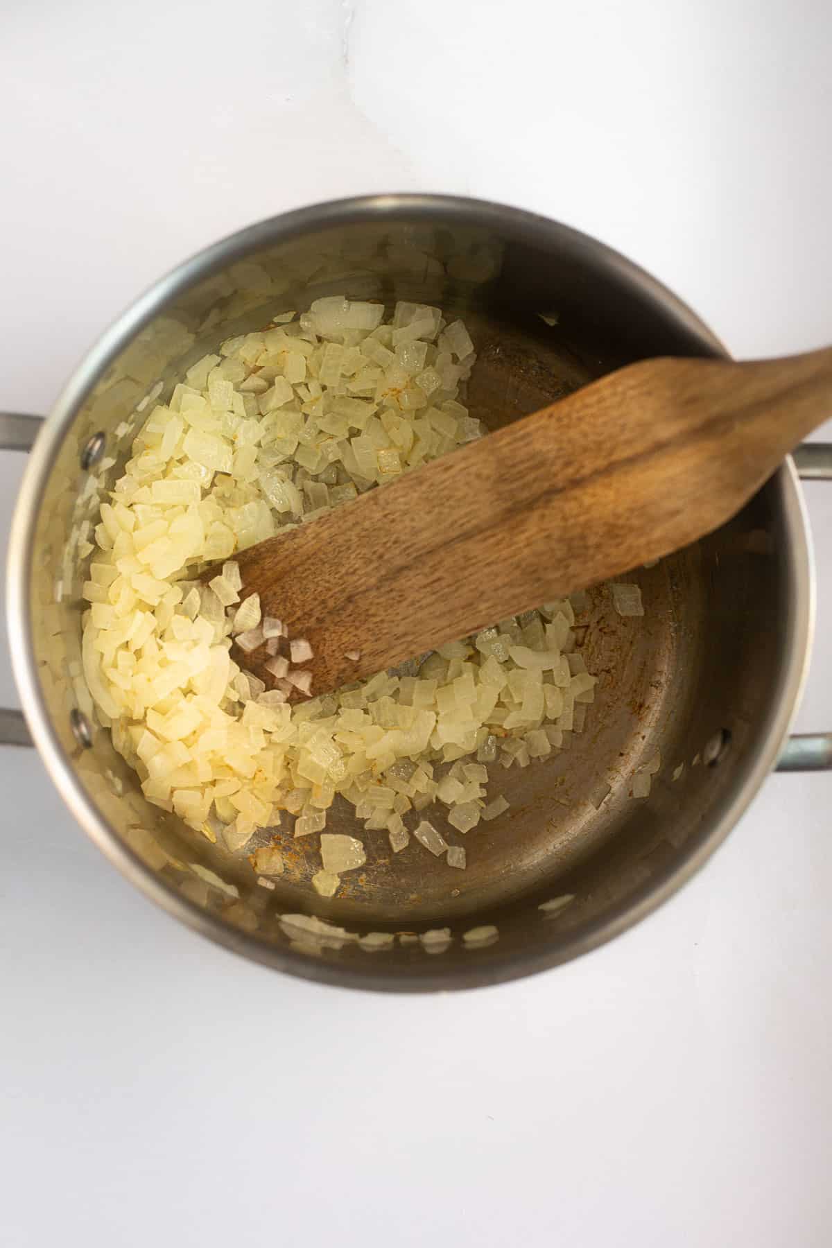 sauteed onions in a silver pot with a wooden spoon.