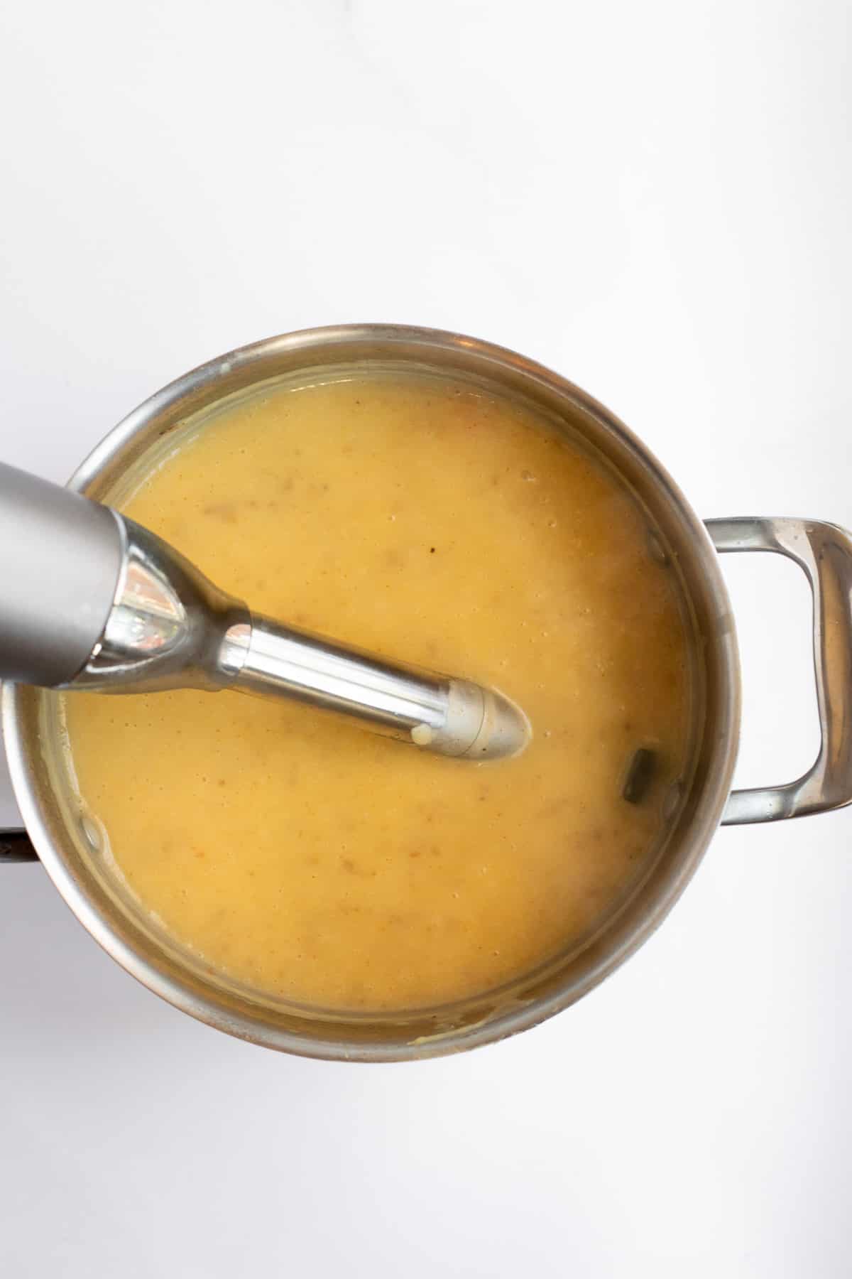 healthy potato soup in a silver pot with an immersion blender.