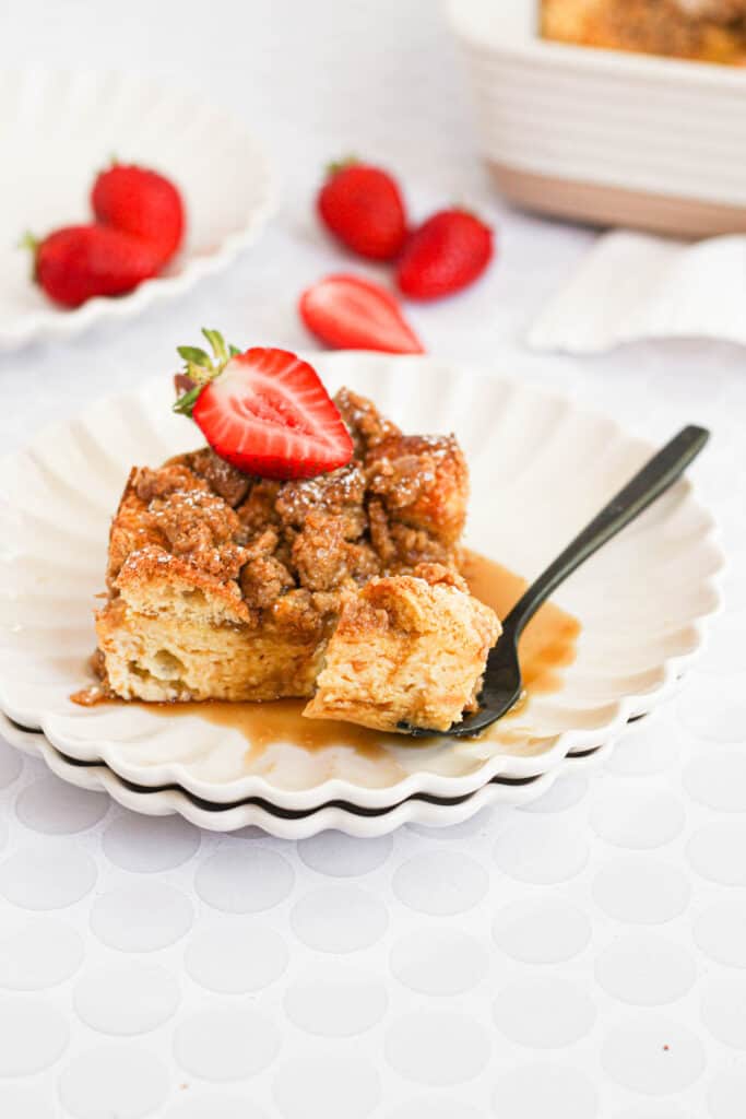piece of brioche french toast casserole on white plate with strawberries and syrup.