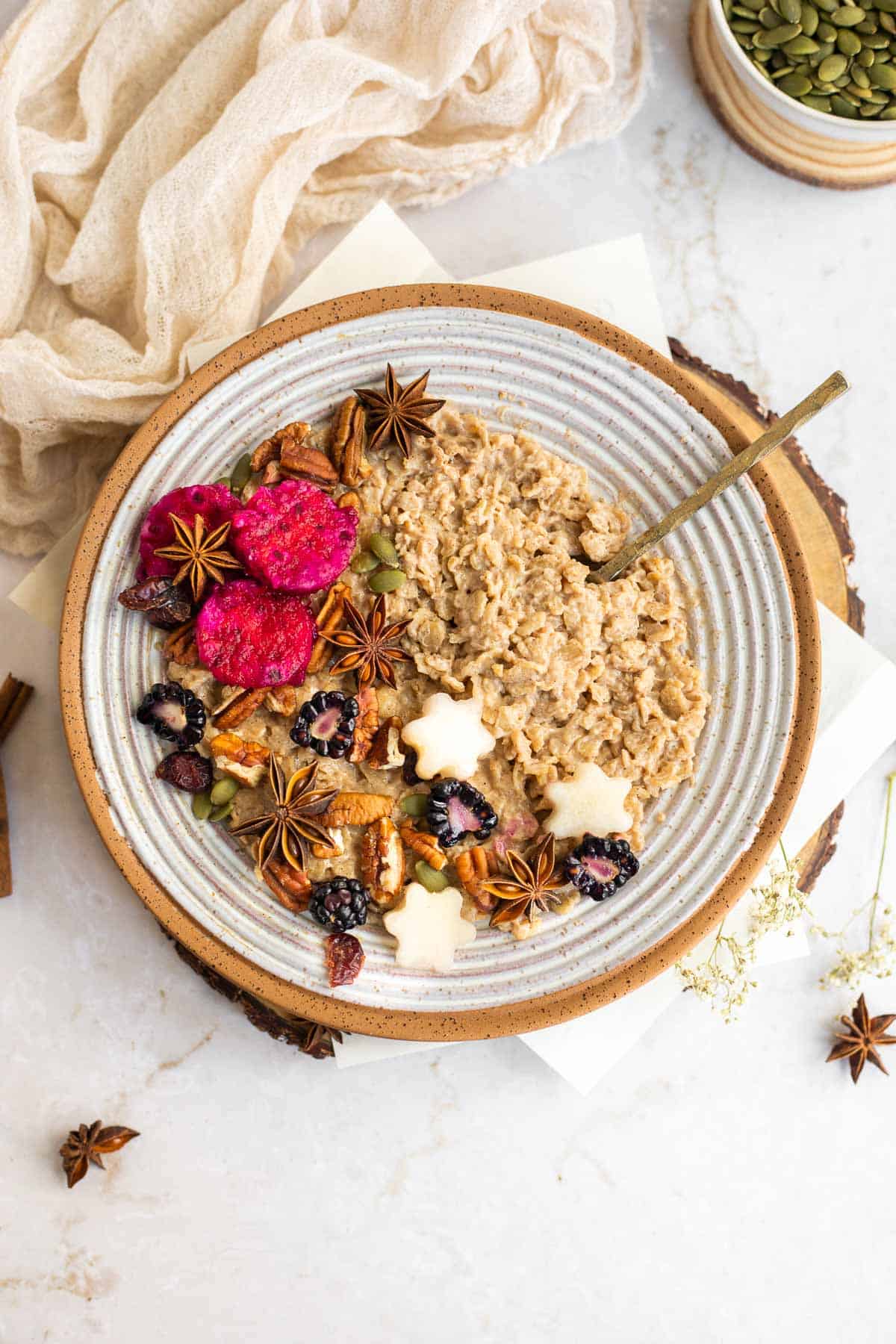 cinnamon oatmeal in a gray bowl with fruit, nuts, and star anise as toppings.