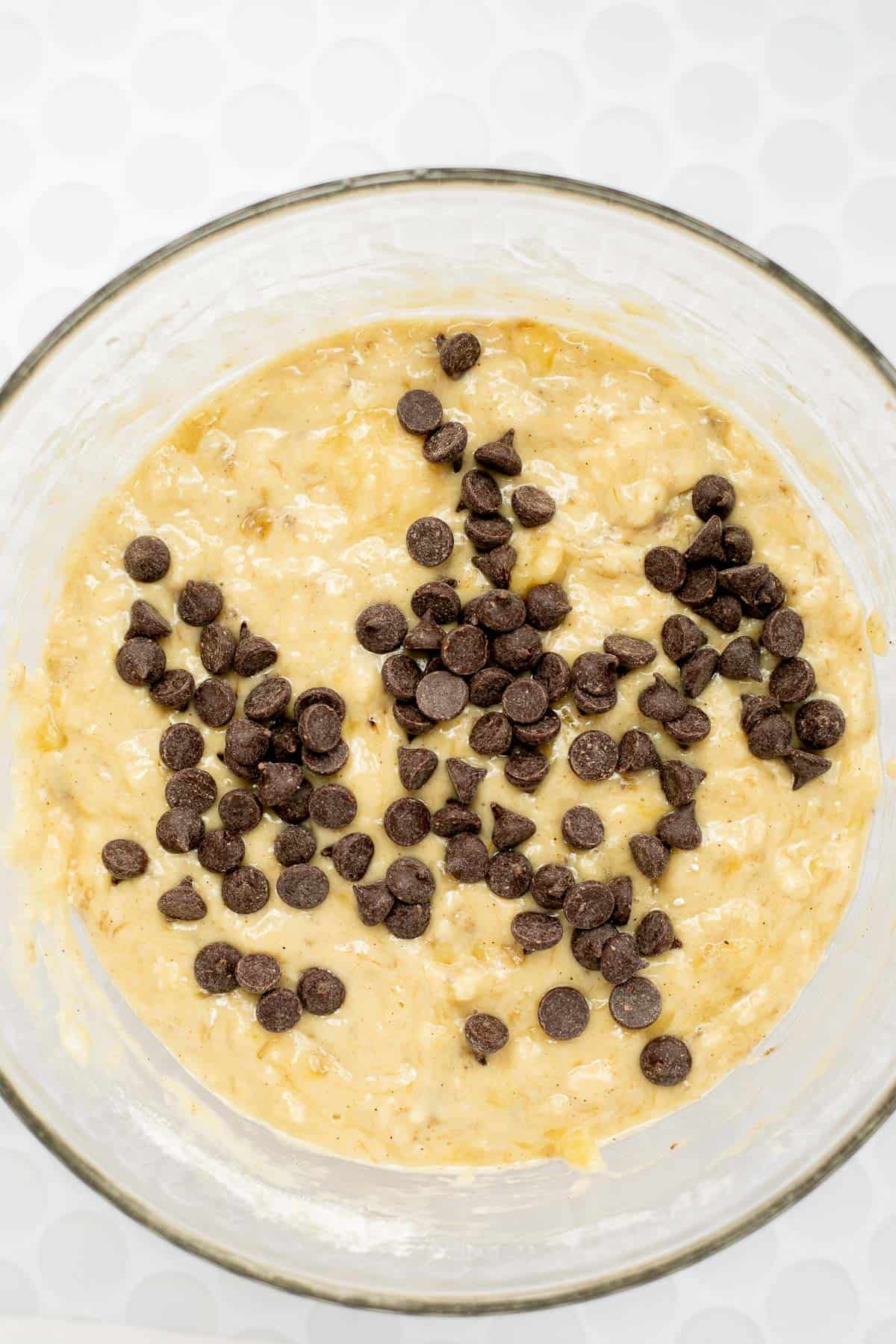 chocolate chips on banana bread batter in a glass bowl.