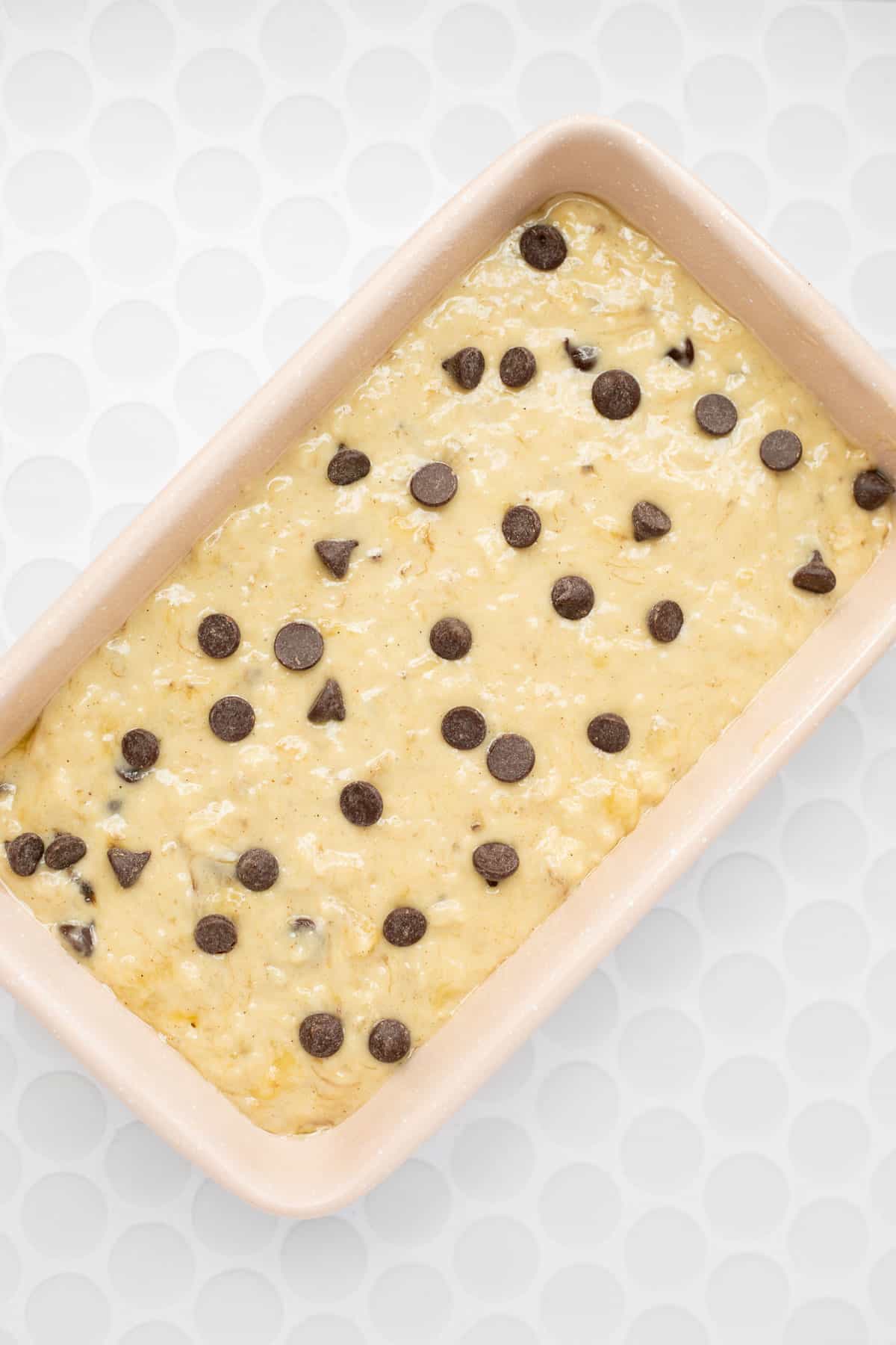 healthy banana bread batter in pink loaf pan topped with chocolate chips.