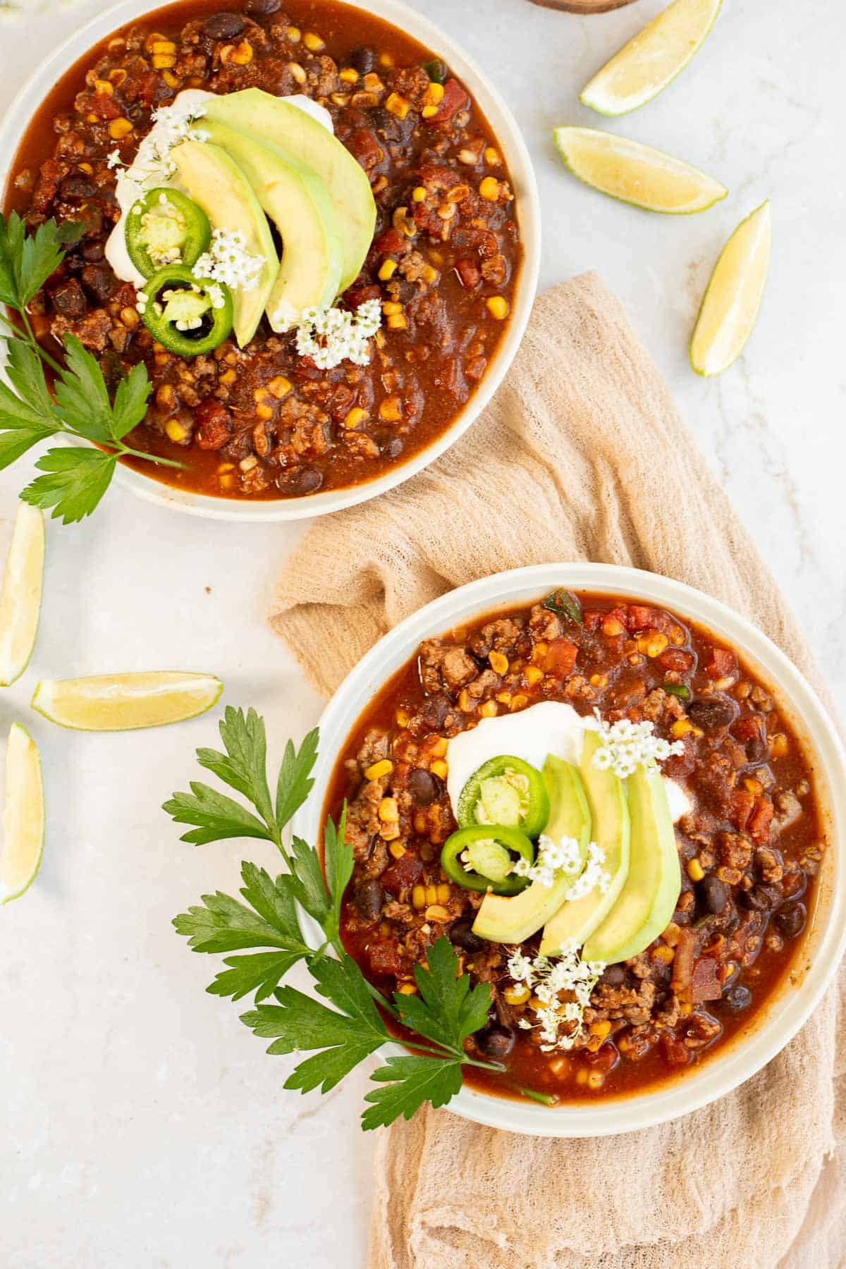 overhead shot of two bowls of gluten free chili with avocado and lime slices.