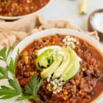 gluten free chili in white bowls topped with avocado and cilantro.