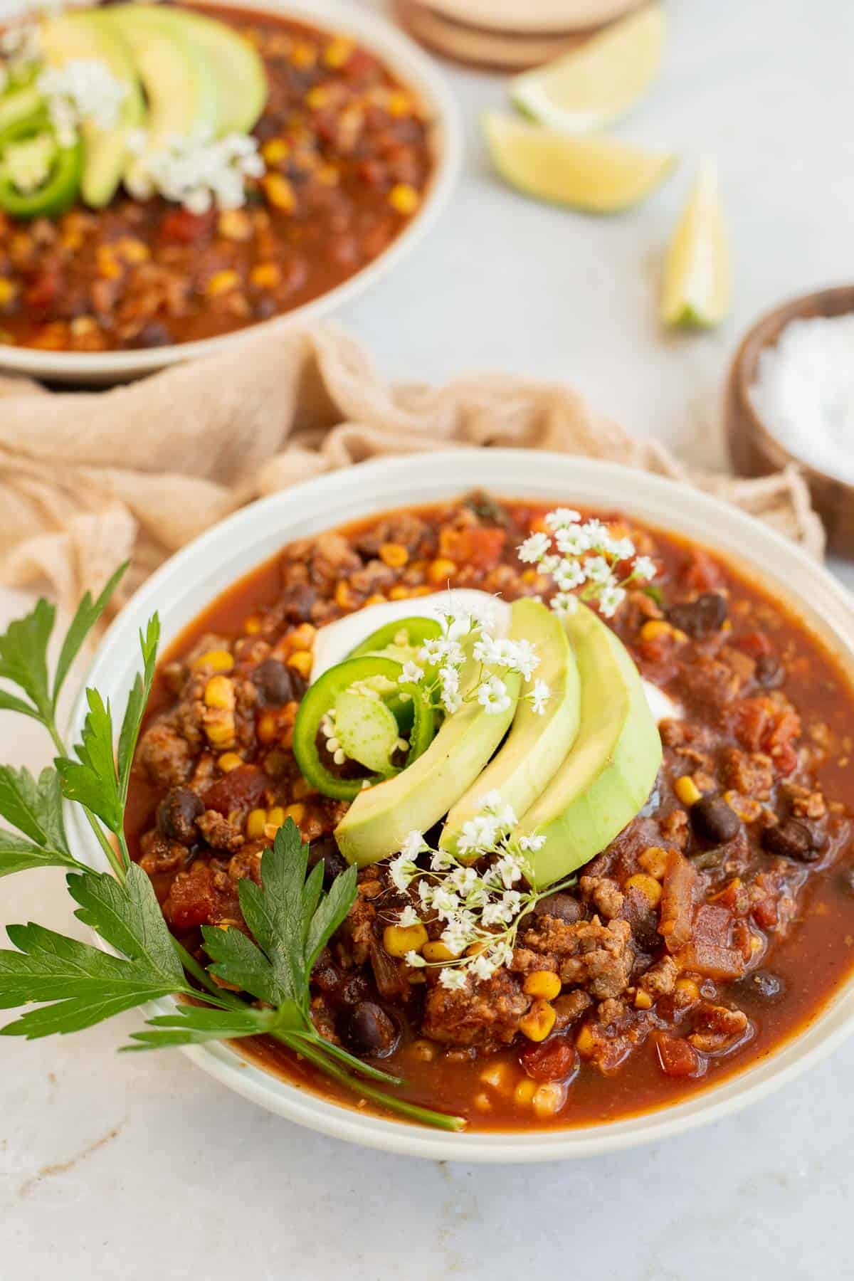 gluten free chili in white bowls topped with avocado and cilantro.