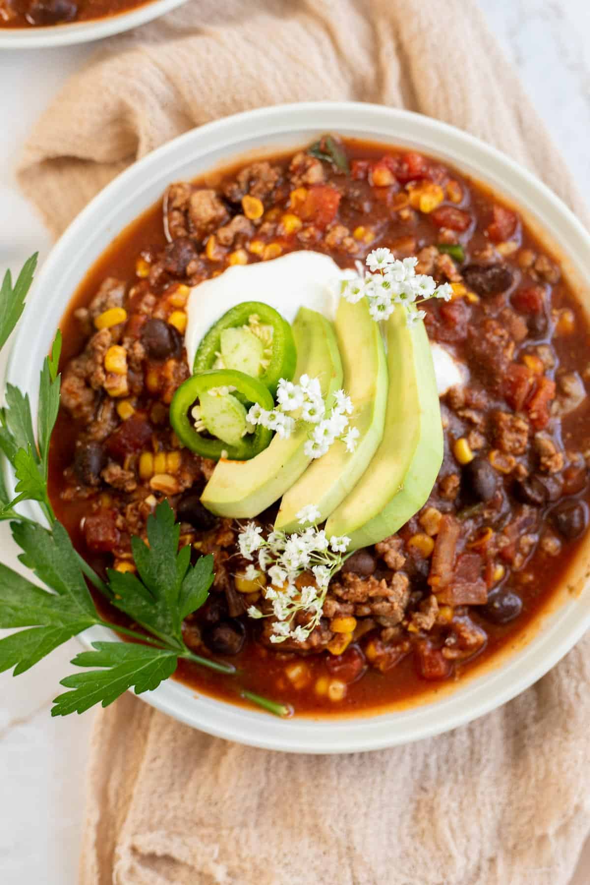 healthy chili in white bowl with sour cream, jalapenos, and avocado slices.