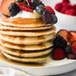 oat milk pancakes stacked with berries, yogurt, and syrup on top.