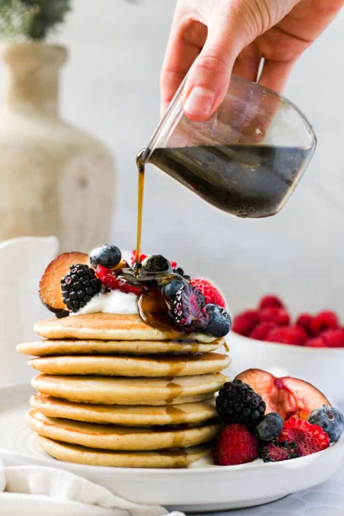 maple syrup being poured over a stack on oat milk pancakes.