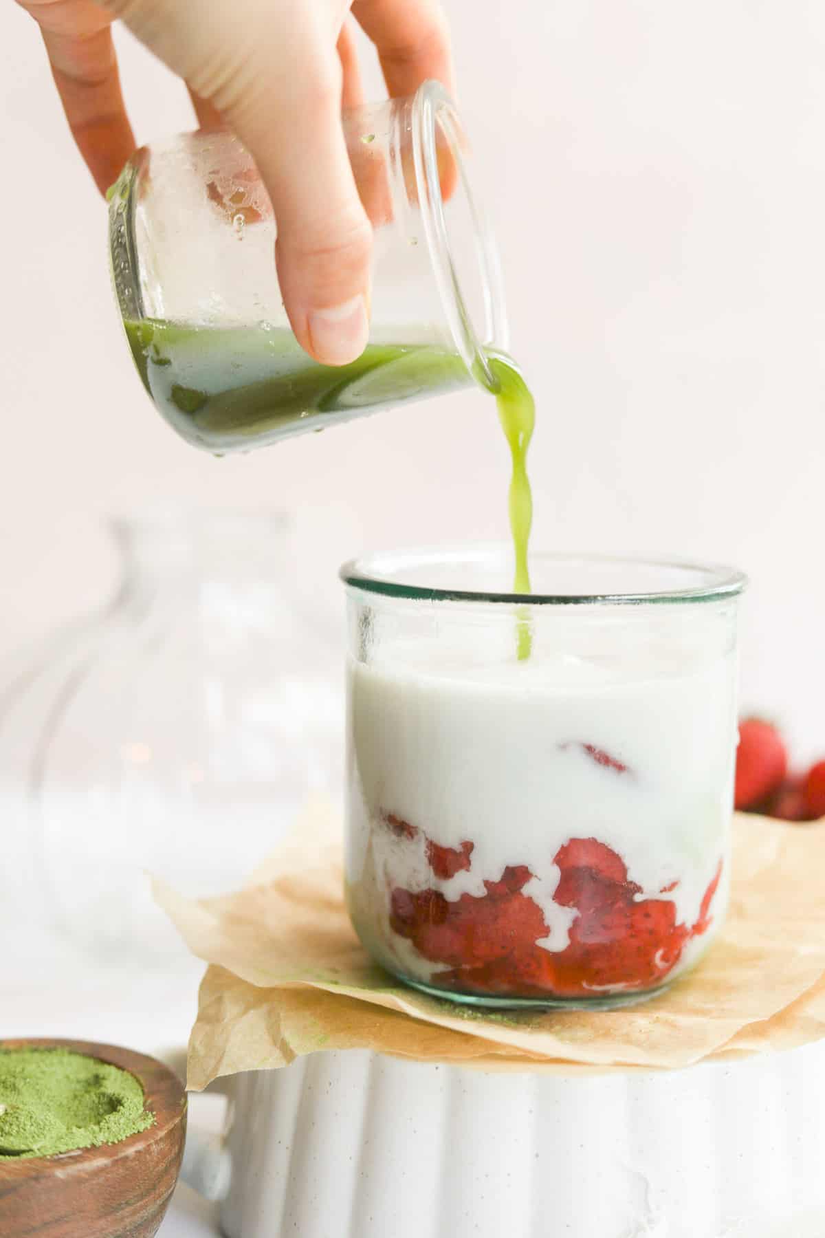matcha being poured over a glass of milk and strawberries.