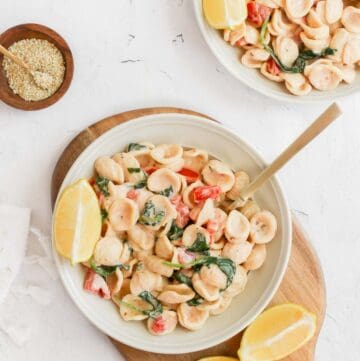 tahini pasta in a white bowl with lemon wedge and gold cutlery.