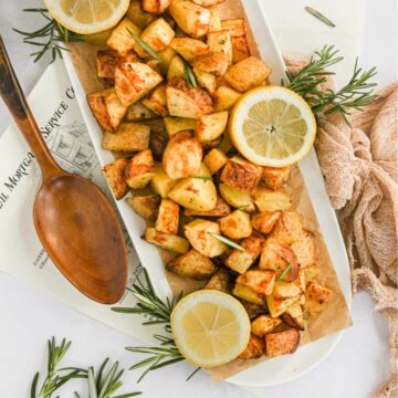 air fryer diced potatoes on white platter with lemon and rosemary.