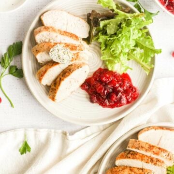 air fryer turkey tenderloin on white plates with butter, cranberry sauce, and salad.