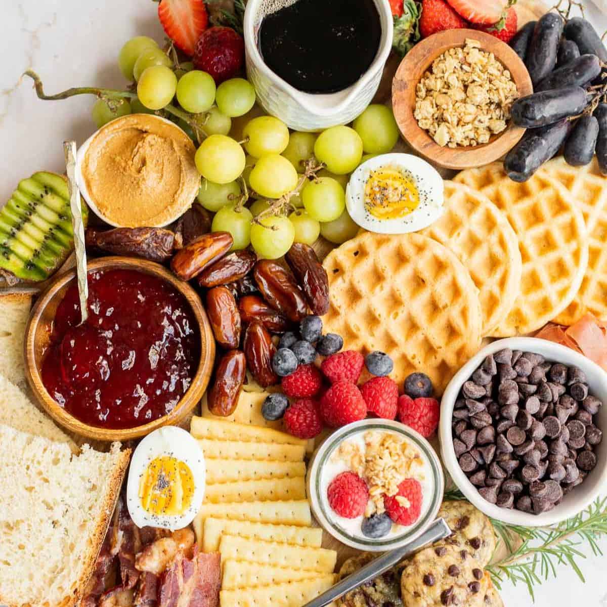 breakfast charcuterie board with waffles, fruit, meats, and spreads on a wooden board.