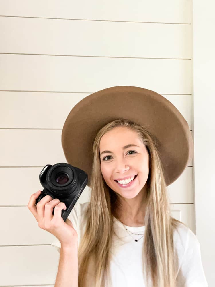 girl in white shirt wearing brown hat holding a camera.