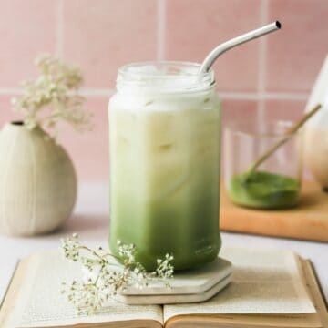oat milk matcha latte in glass with straw and flowers.