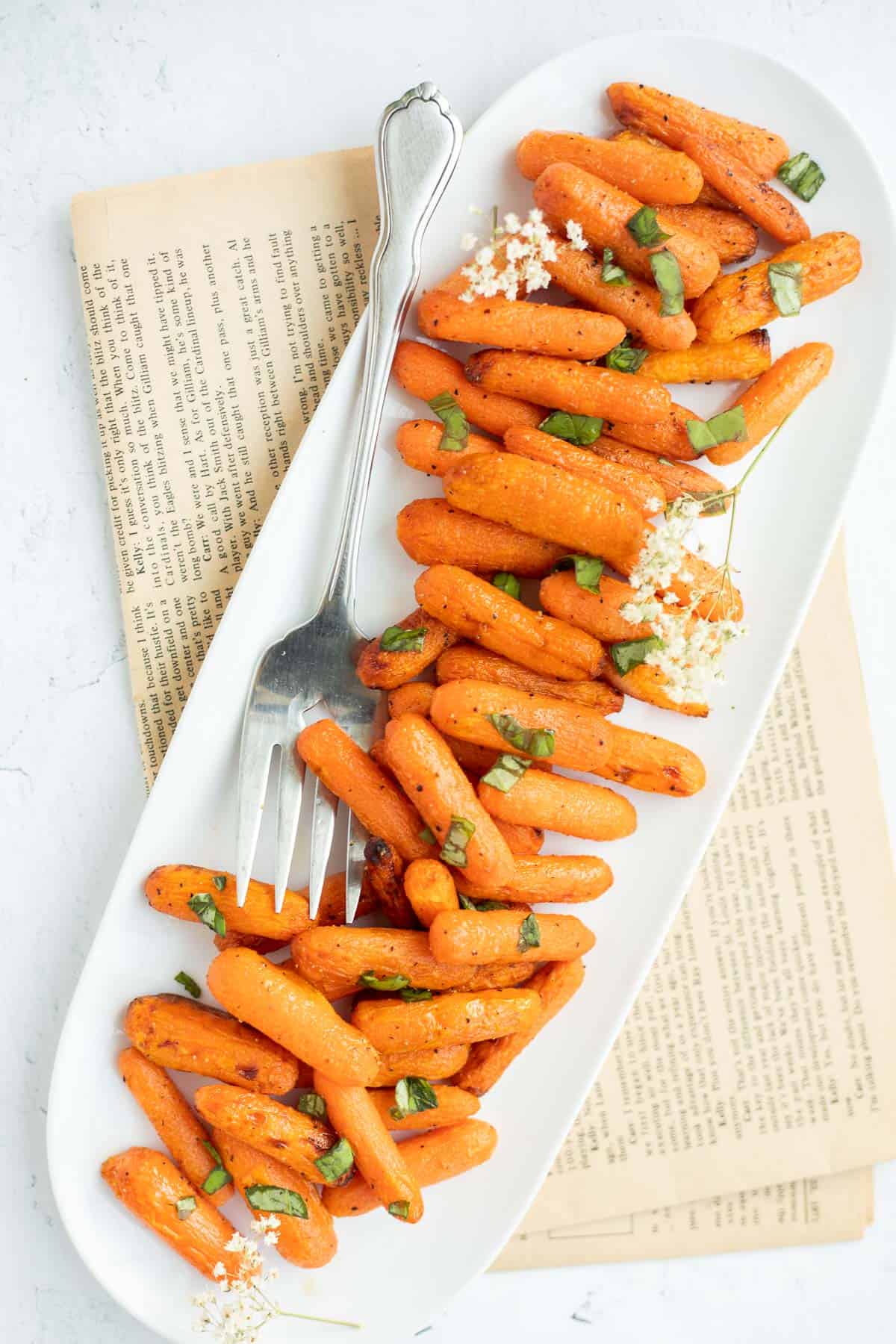 baby carrots roasted in air fryer on a white platter topped with herbs.