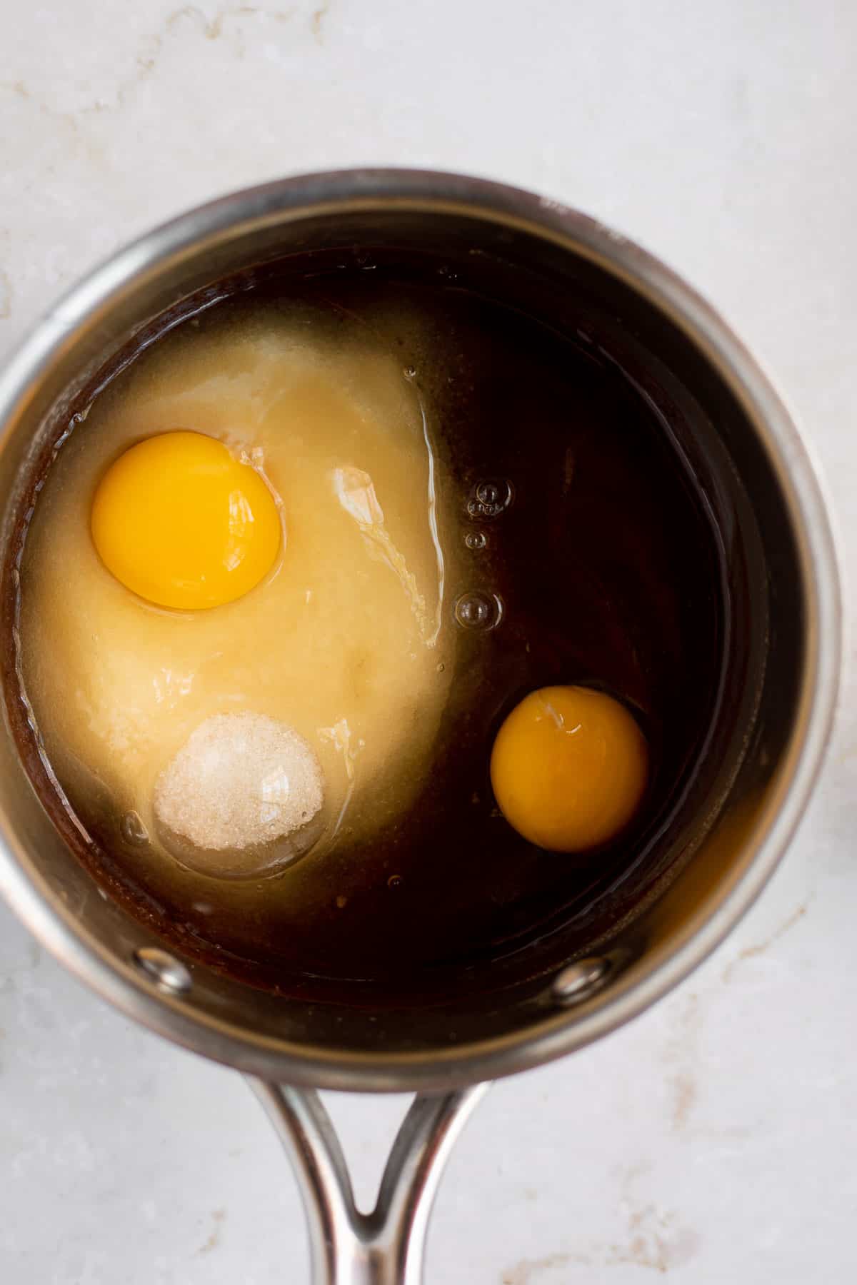 2 eggs and sugar on top of melted chocolate mixture in a pot.