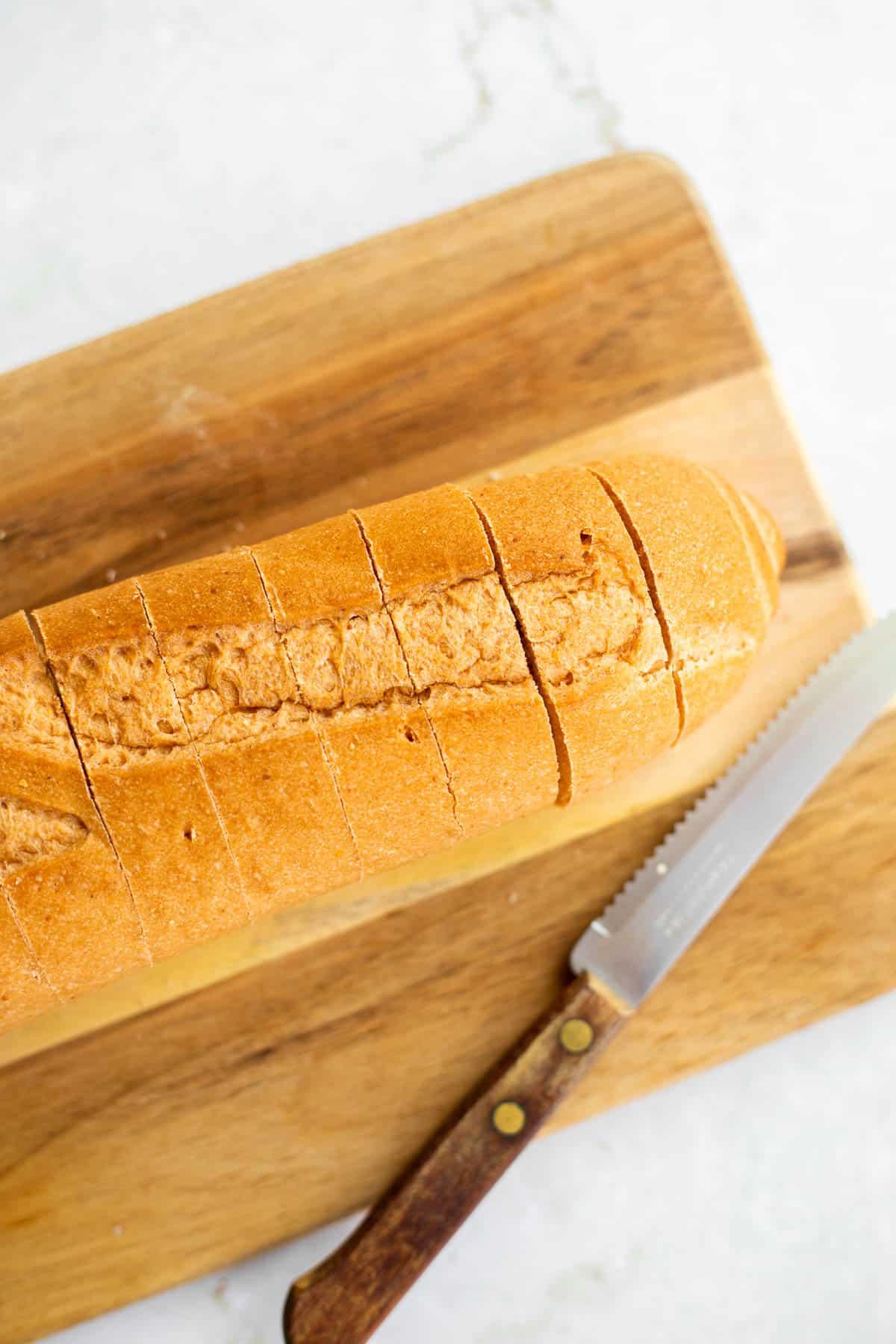 gluten free baguette cut like an accordion on a wooden cutting board.