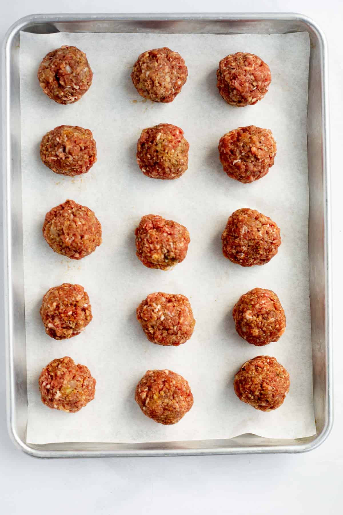 raw healthy meatballs rolled into balls on a baking sheet.