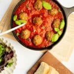 gluten free meatballs in a castiron pan with sauce and basil.