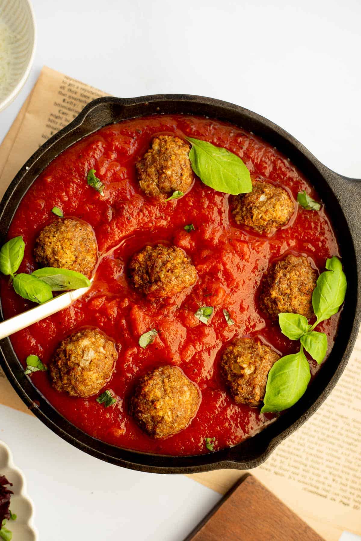 gluten free meat balls in a cast iron skillet with tomato sauce and fresh basil leaves.