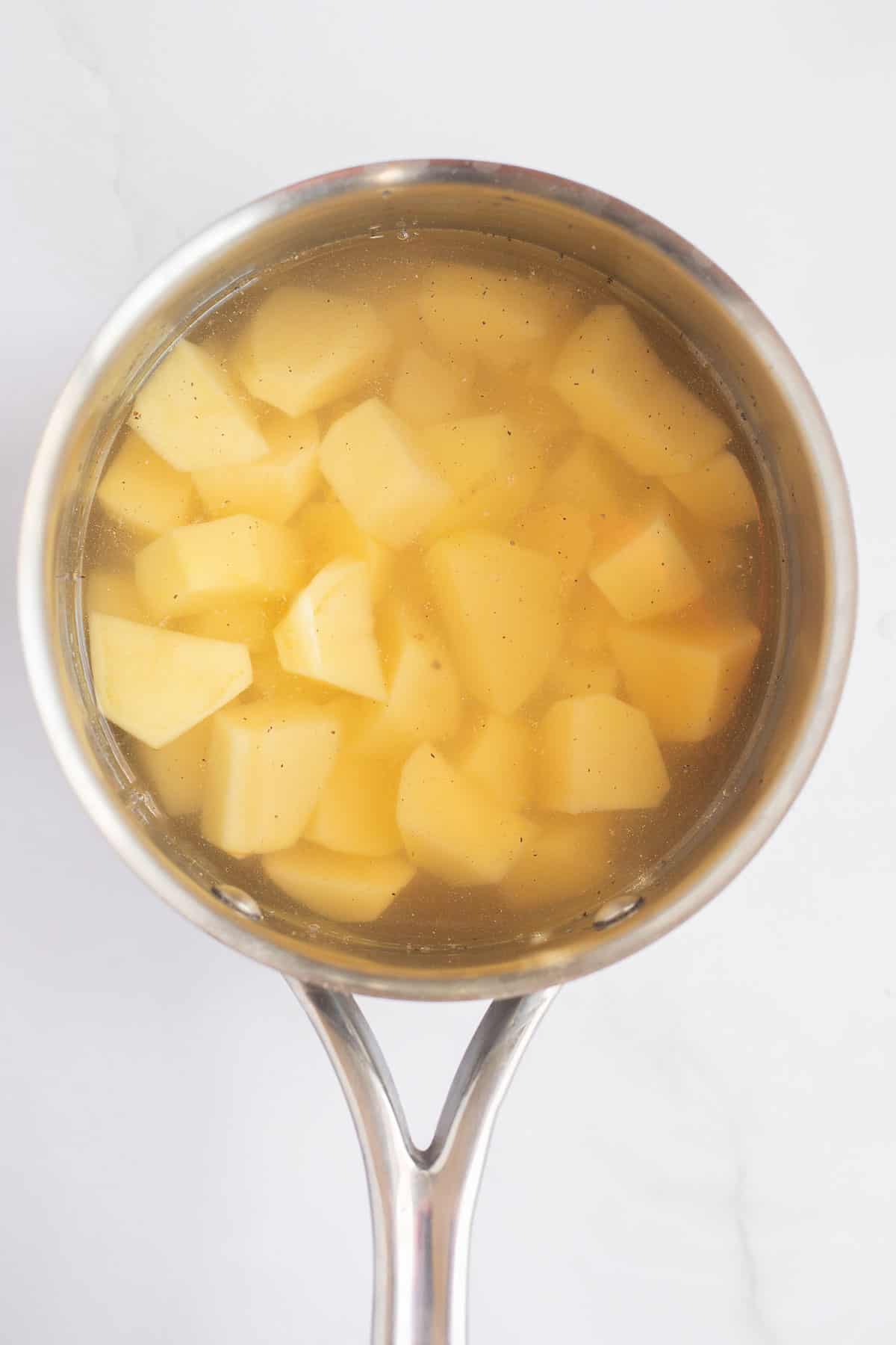 potato chunks in a silver pot of water.