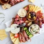 small charcuterie board full of meats, cheese, and vegetables on a white backdrop.