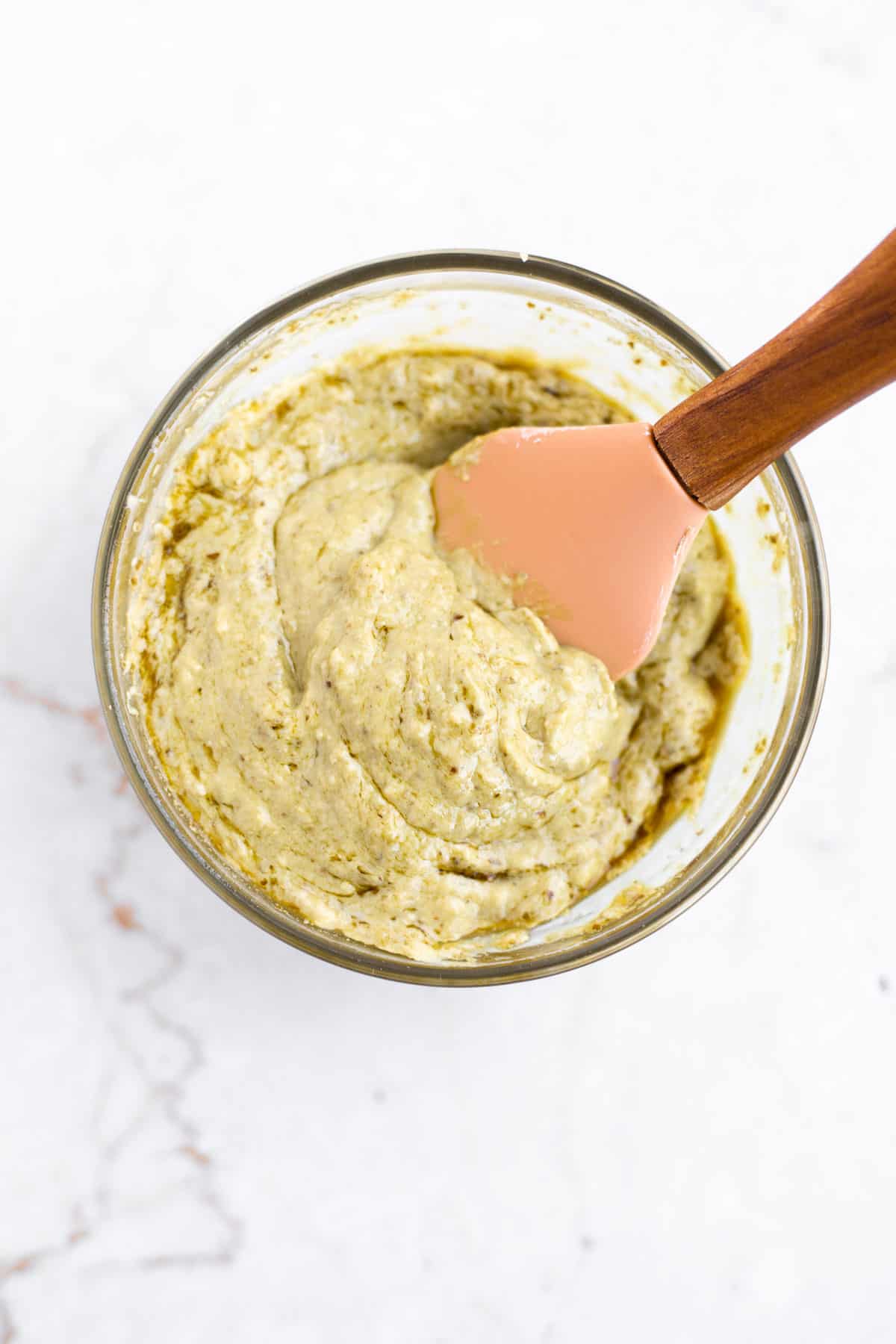 pesto mayo in a glass bowl with a small pink spatula.