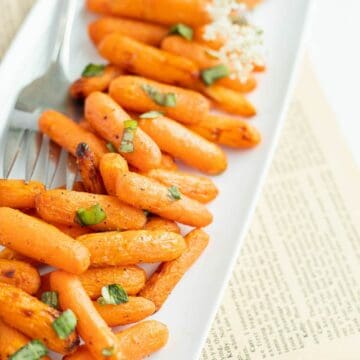 air fryer carrots sprinkled with herbs on a white platter.