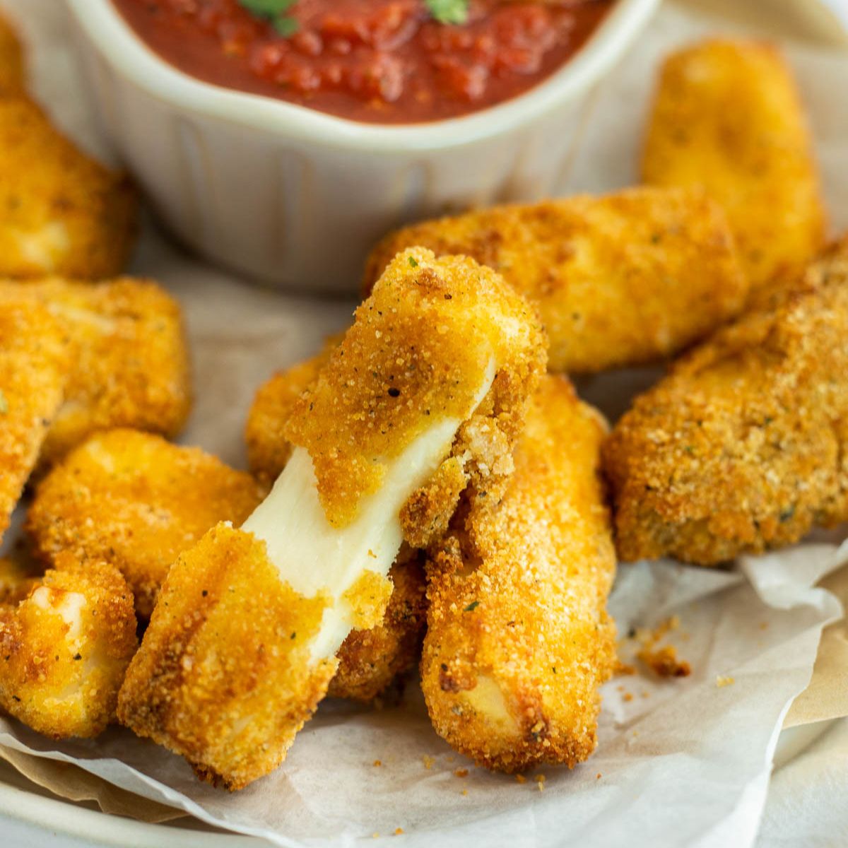 gluten free mozzarella sticks with cheese melting out of one on a white plate.