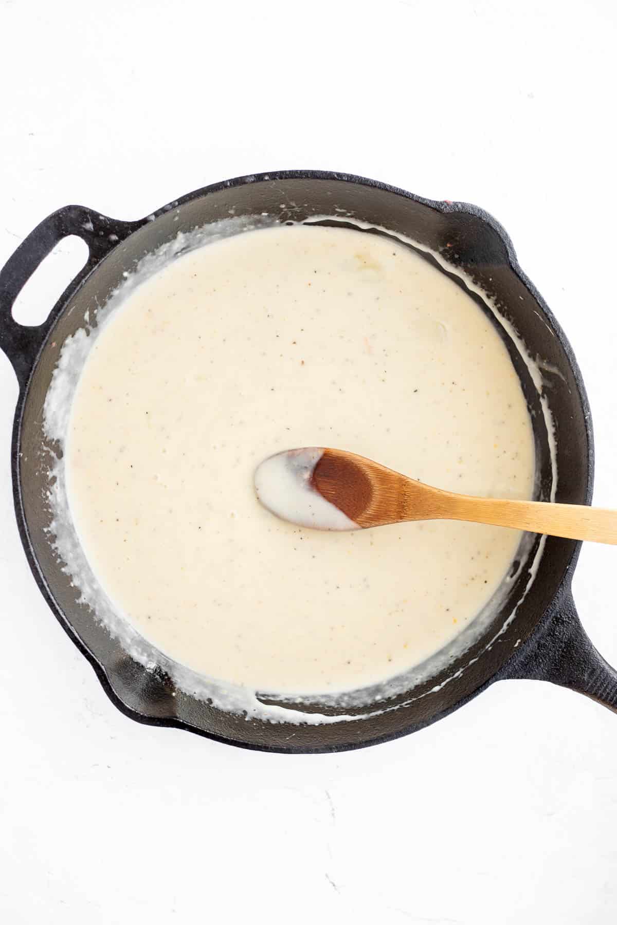 cheese sauce in cast iron pan with a wooden spoon.