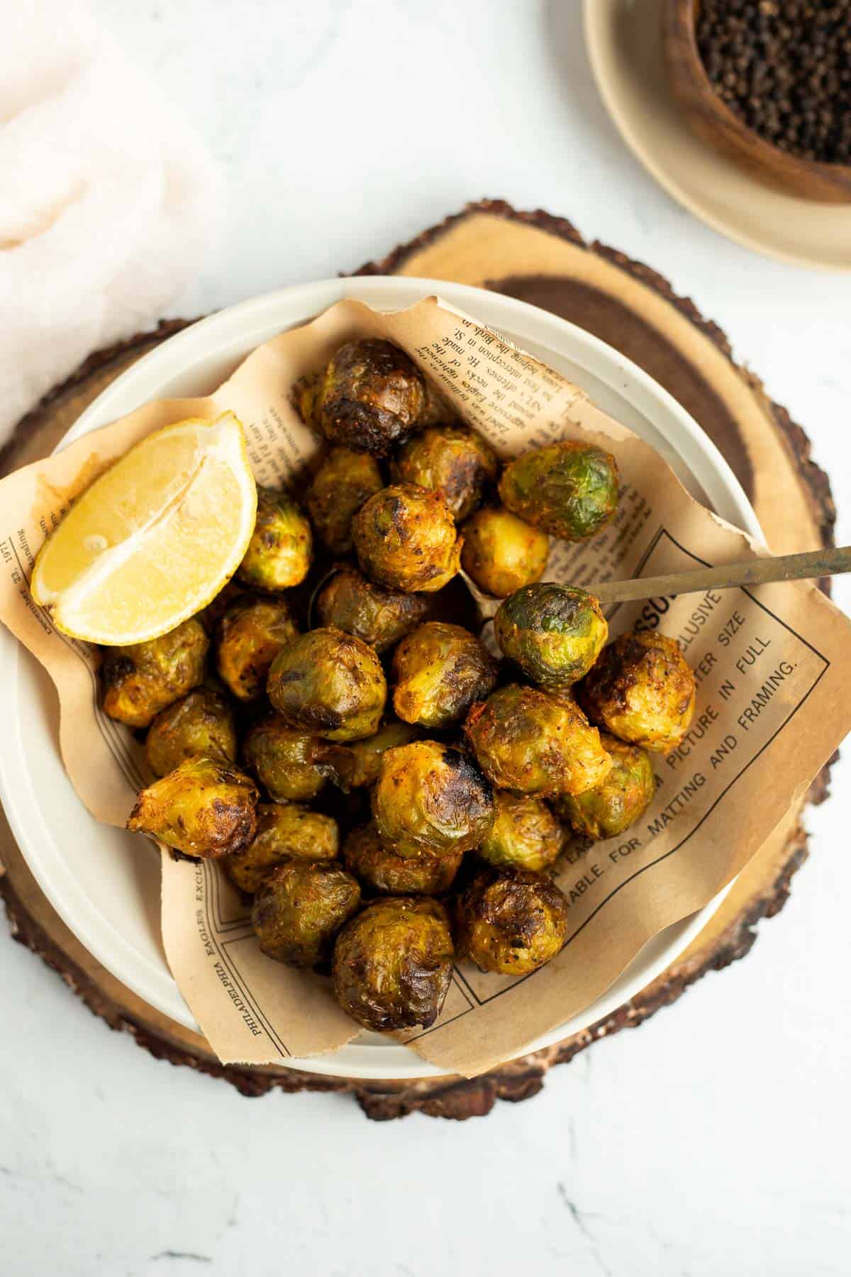 Air Fryer Frozen Brussels Sprouts in a white bowl with a lemon wedge and gold spoon.