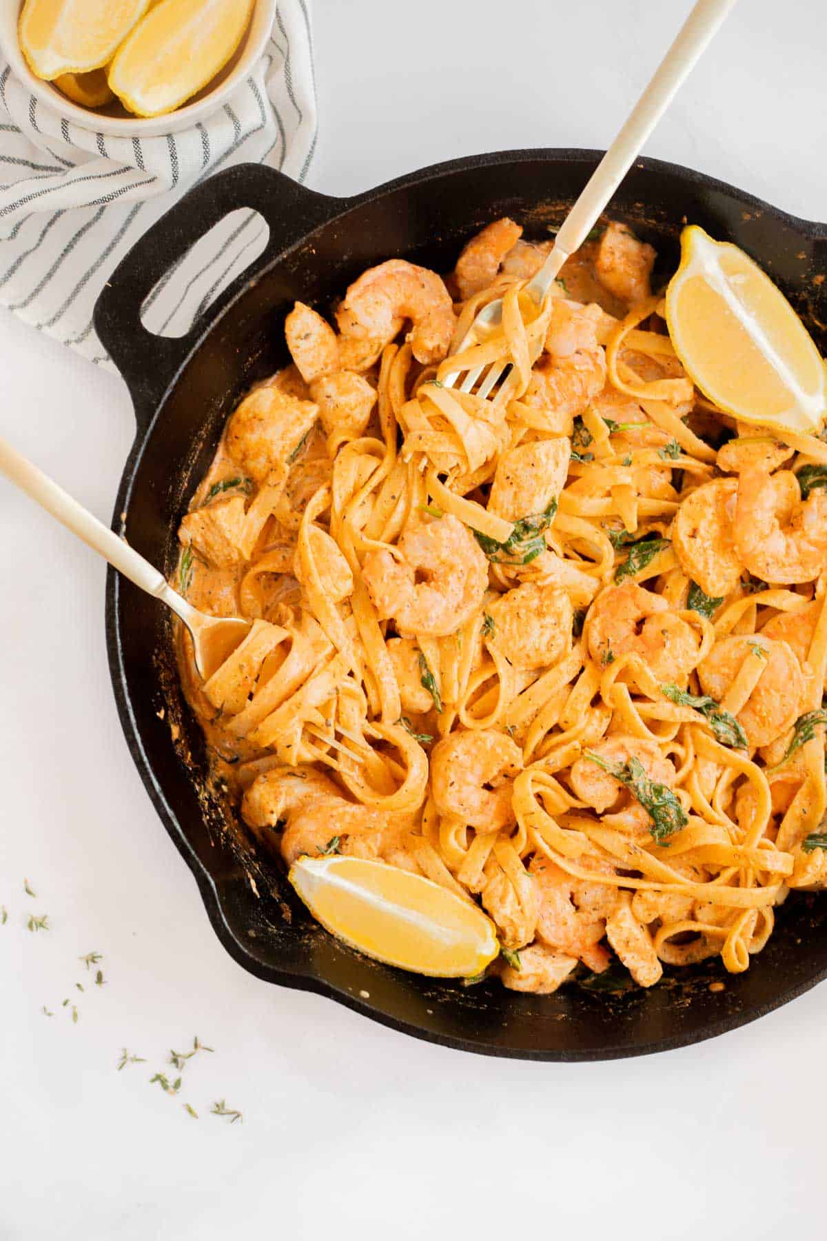 cajun chicken and shrimp pasta in a cast iron skillet with two gold forks.