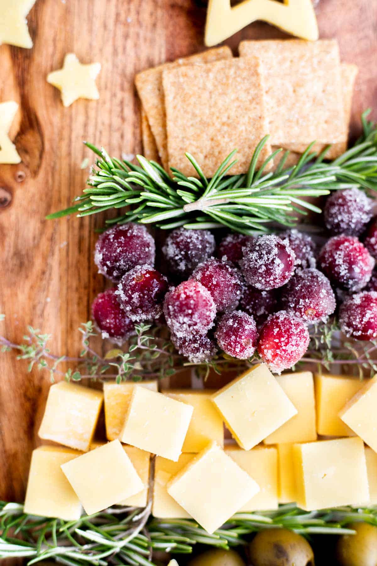 sugared cranberries and cheese cubes with fresh herbs on a Christmas cheese board.