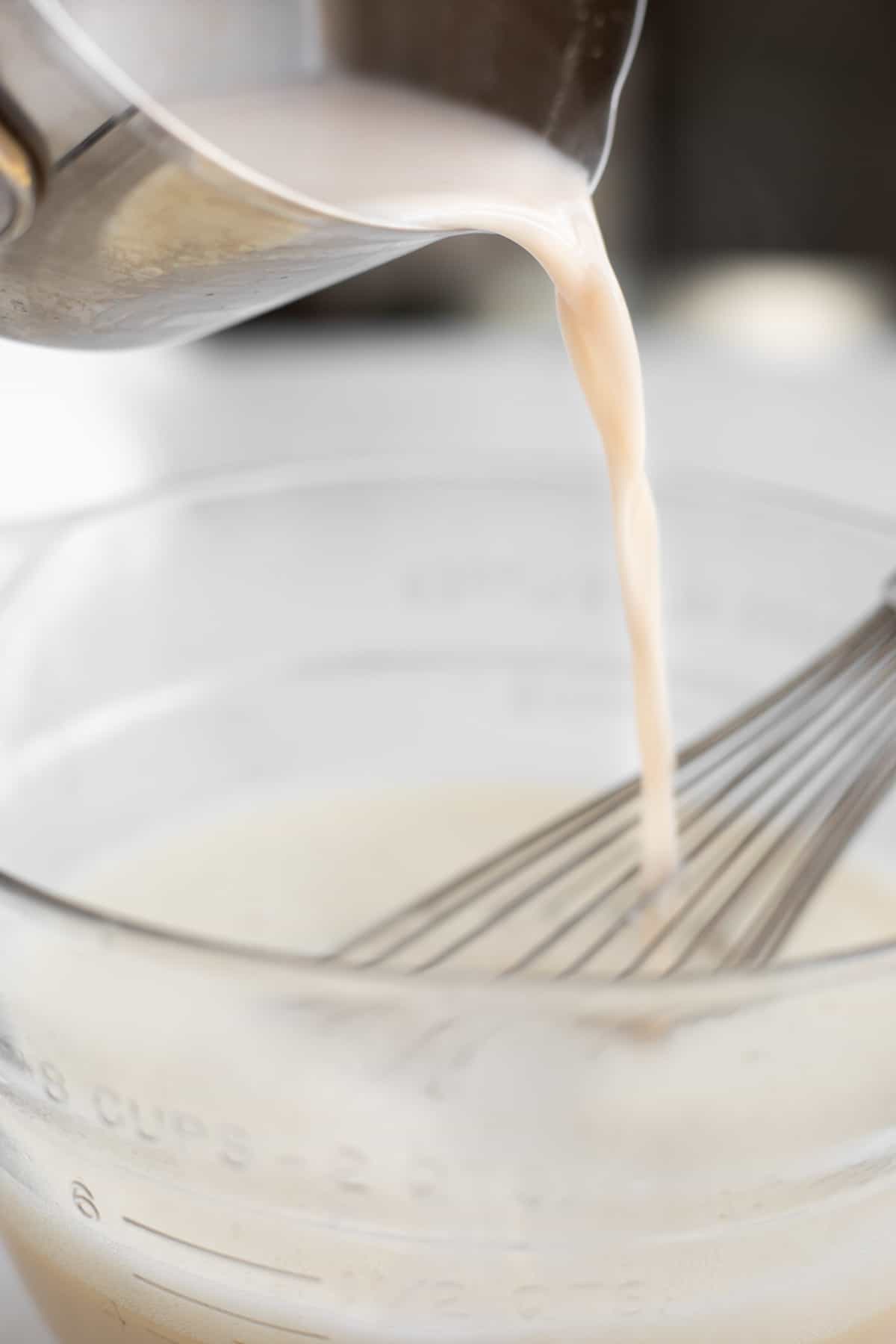 milk pouring into a glass bowl with a whisk.