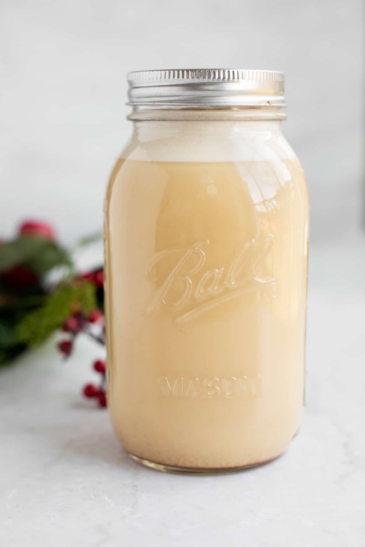 a mason jar of dairy free eggnog on a white backdrop.