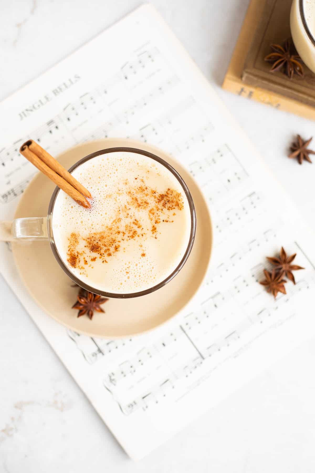 a mug of dairy free eggnog with a cinnamon stick on a sheet of music.