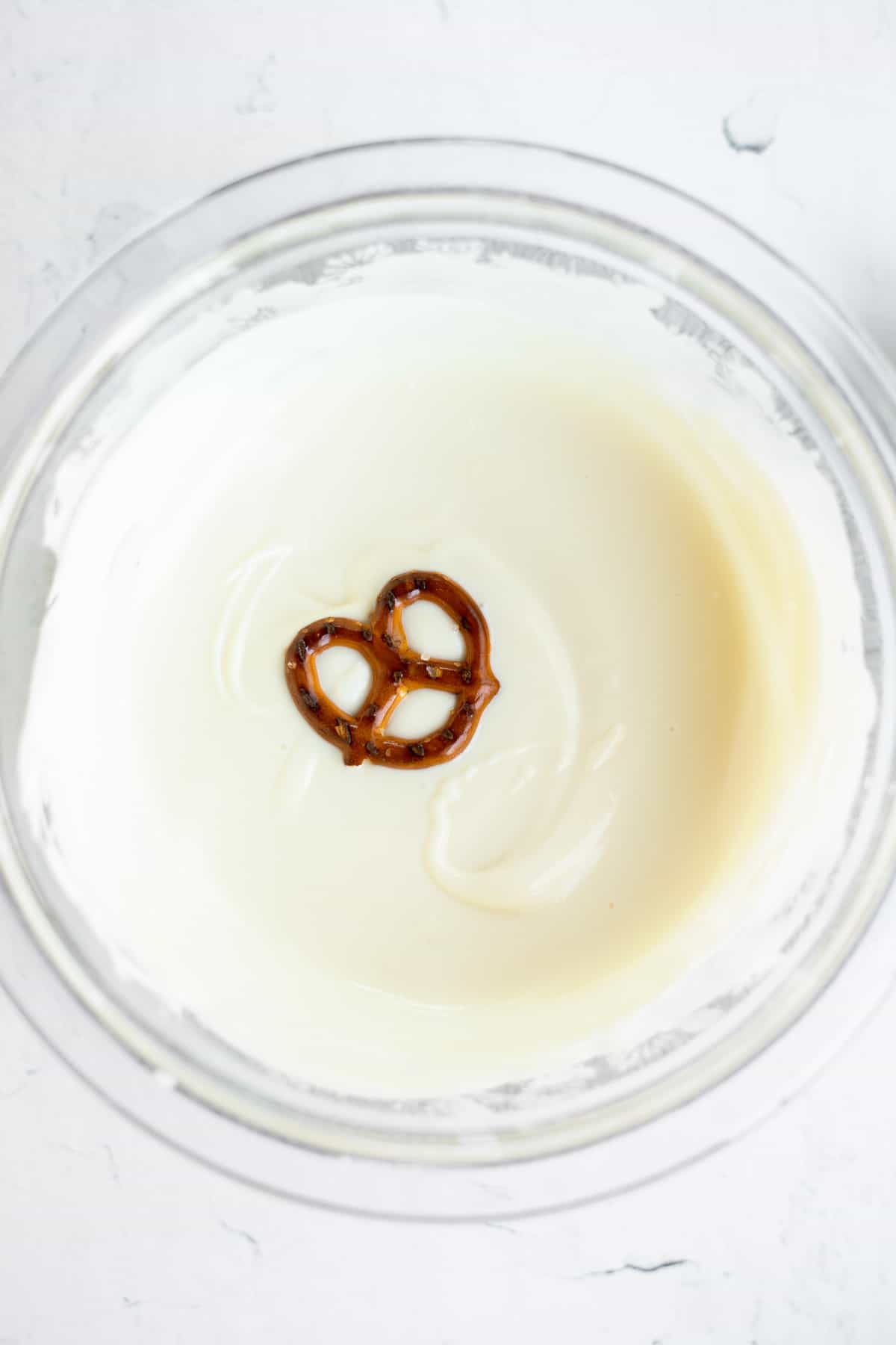 mini pretzel twist in a small bowl of melted white chocolate.
